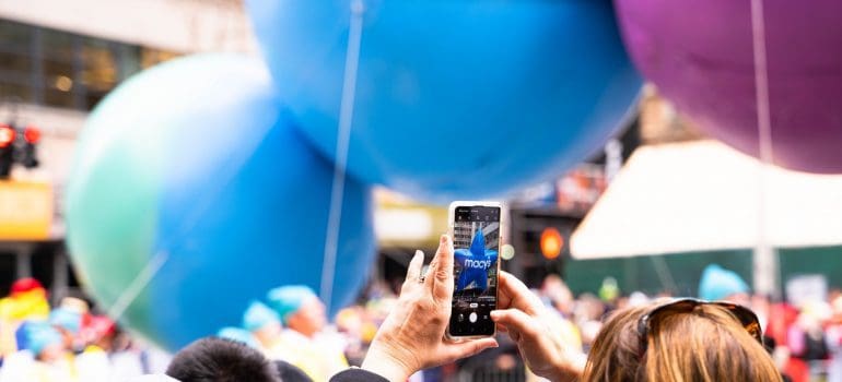 Woman holding the phone up on Macy's Thanksgiving Day Parade