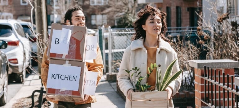 A woman and man walking holding moving boxes